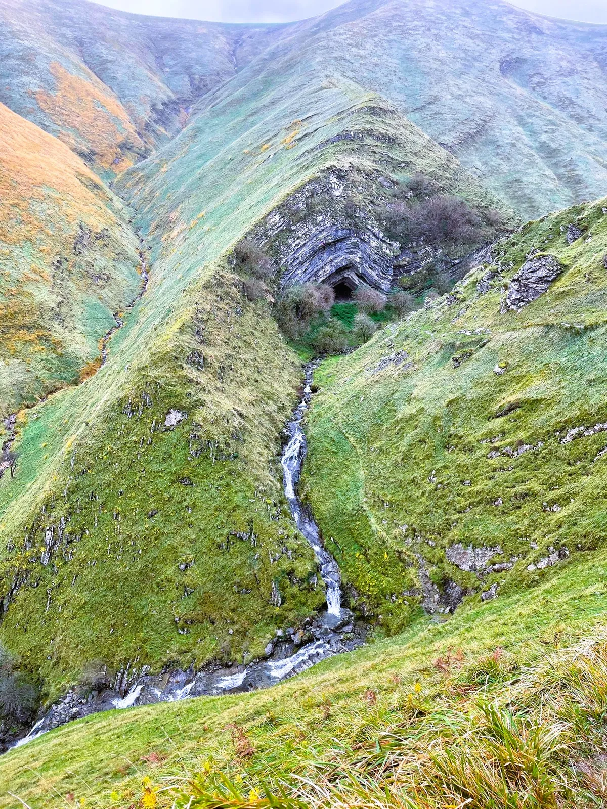 Entrada de la cueva de Arpea entre estratos de roca y laderas verdes